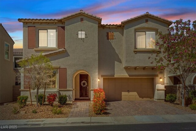 mediterranean / spanish-style house featuring a tiled roof, decorative driveway, a garage, and stucco siding