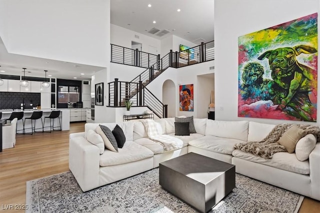living area featuring light wood-style flooring, arched walkways, recessed lighting, stairway, and a high ceiling