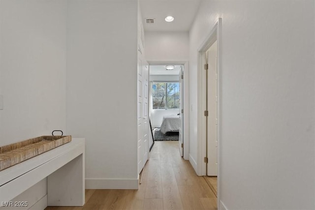 hallway with light wood-style floors, baseboards, and visible vents