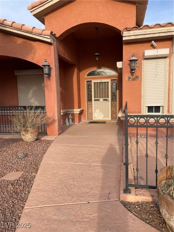 210 Lailani St, Las Vegas, NV 89110 - view of exterior entry with stucco siding, a tiled roof, and a gate