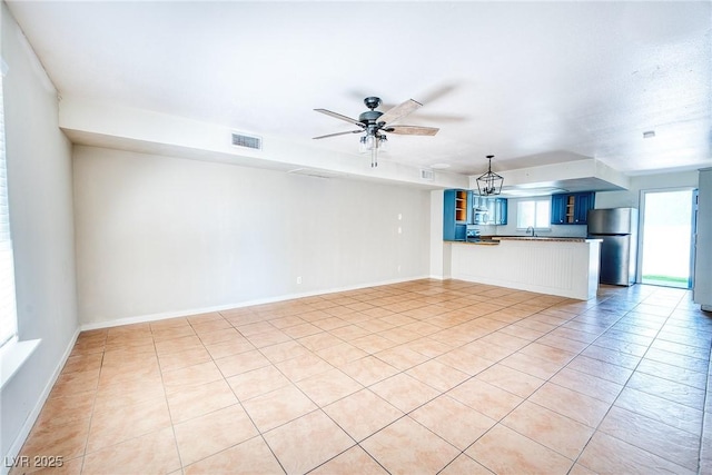 unfurnished living room with baseboards, light tile patterned floors, a ceiling fan, visible vents, and a sink