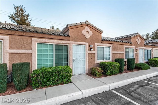 townhome / multi-family property with a tile roof, uncovered parking, and stucco siding