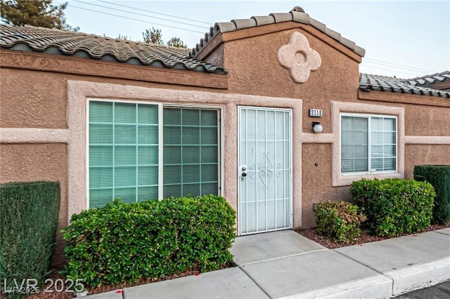 doorway to property featuring a tile roof and stucco siding
