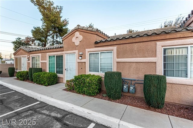 multi unit property with a tile roof, uncovered parking, and stucco siding