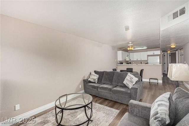living room featuring visible vents, baseboards, ceiling fan, a textured ceiling, and dark wood-style floors