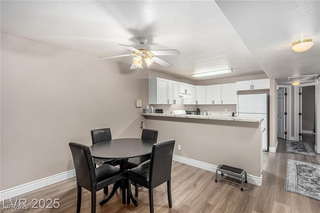 dining space with light wood-style floors, ceiling fan, baseboards, and a textured ceiling