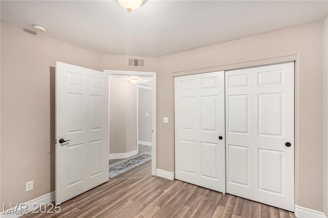 unfurnished bedroom featuring visible vents, a closet, baseboards, and wood finished floors