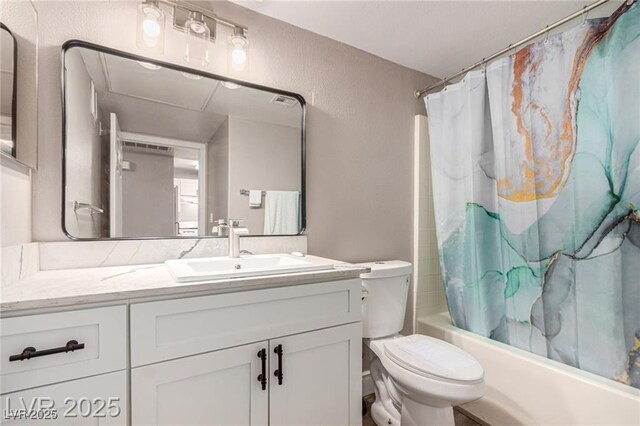 bathroom featuring toilet, shower / bath combo with shower curtain, a textured wall, and vanity