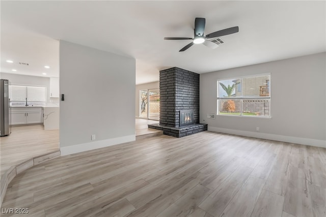 unfurnished living room with light wood-style floors, ceiling fan, baseboards, and a fireplace