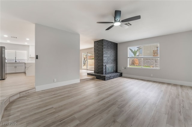 unfurnished living room with plenty of natural light, light wood-style floors, baseboards, and a ceiling fan