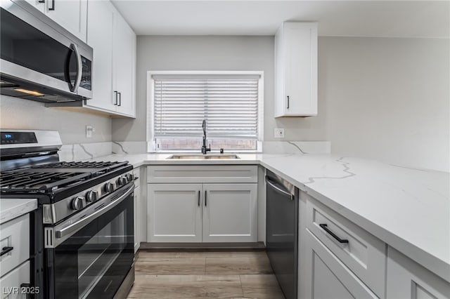 kitchen with white cabinets, light stone countertops, a sink, and appliances with stainless steel finishes