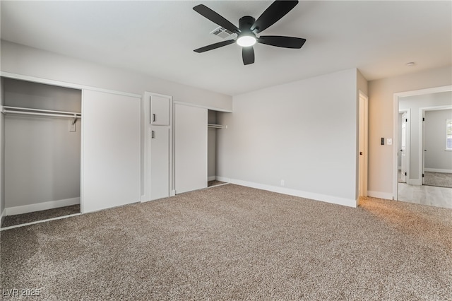 unfurnished bedroom with two closets, ceiling fan, baseboards, and light carpet
