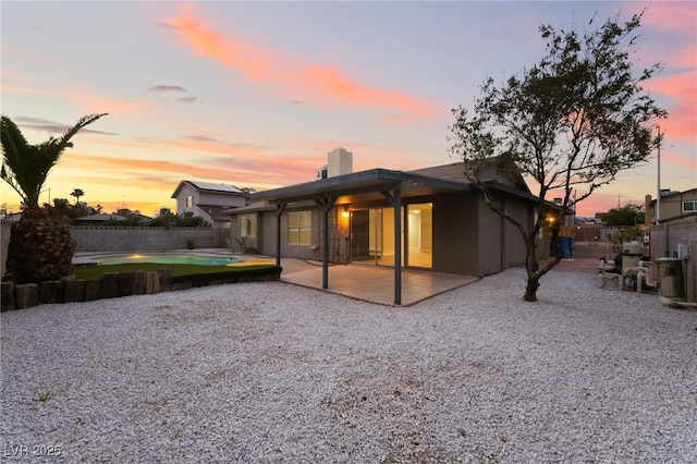 back of house at dusk with a patio, stucco siding, and fence