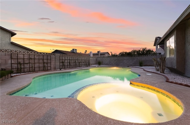 pool at dusk featuring a fenced backyard and a pool with connected hot tub