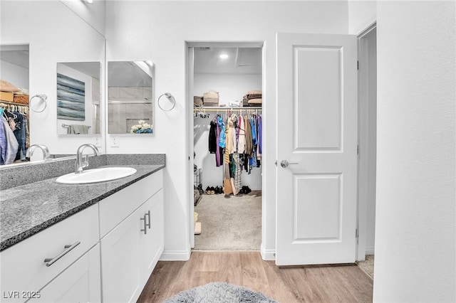 full bath with a walk in closet, a shower stall, wood finished floors, vanity, and baseboards