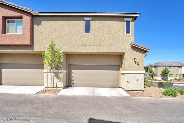 townhome / multi-family property featuring a tiled roof, a garage, driveway, and stucco siding