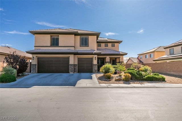 prairie-style home with stone siding, a garage, fence, concrete driveway, and stucco siding