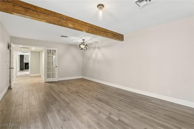 unfurnished room featuring visible vents, wood finished floors, and beamed ceiling