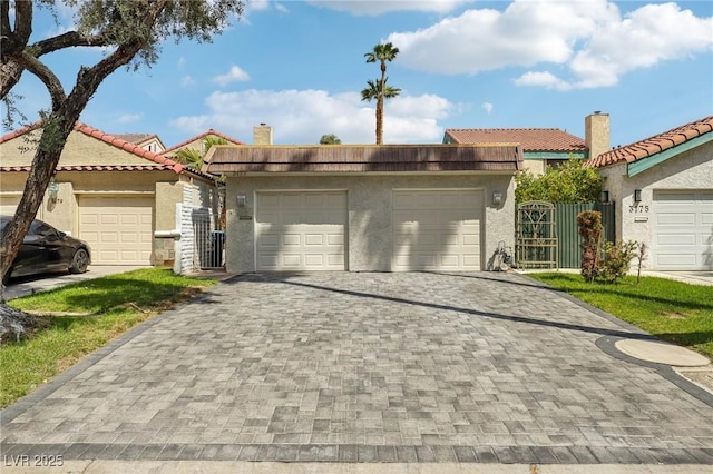 view of front of house featuring an attached garage, a chimney, stucco siding, a gate, and decorative driveway
