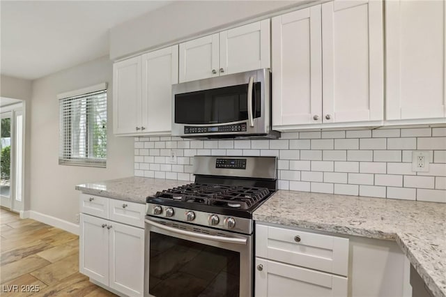 kitchen featuring white cabinets, baseboards, appliances with stainless steel finishes, light stone countertops, and decorative backsplash
