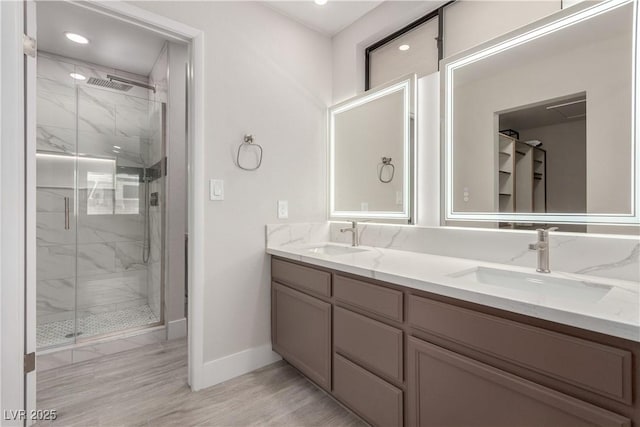 full bathroom featuring a sink, baseboards, a marble finish shower, and double vanity