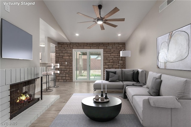 living room with visible vents, a warm lit fireplace, light wood-type flooring, a ceiling fan, and high vaulted ceiling