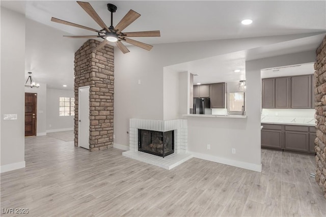 unfurnished living room featuring baseboards, a brick fireplace, ceiling fan, light wood-type flooring, and vaulted ceiling