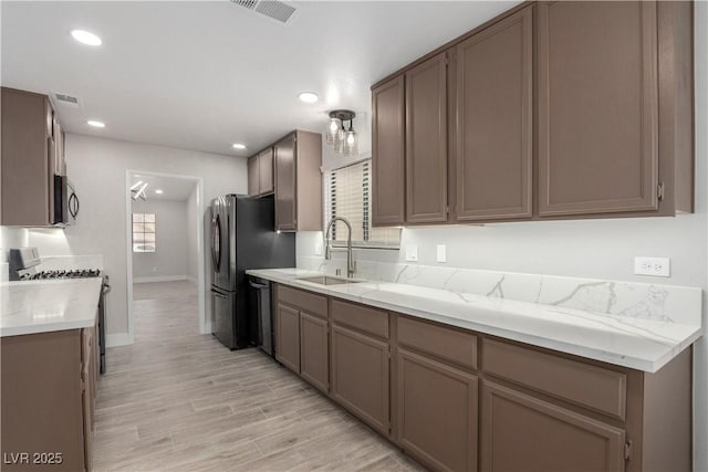 kitchen with light wood-type flooring, visible vents, gas range, stainless steel microwave, and a sink