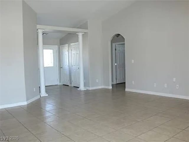 empty room featuring decorative columns, arched walkways, baseboards, and vaulted ceiling