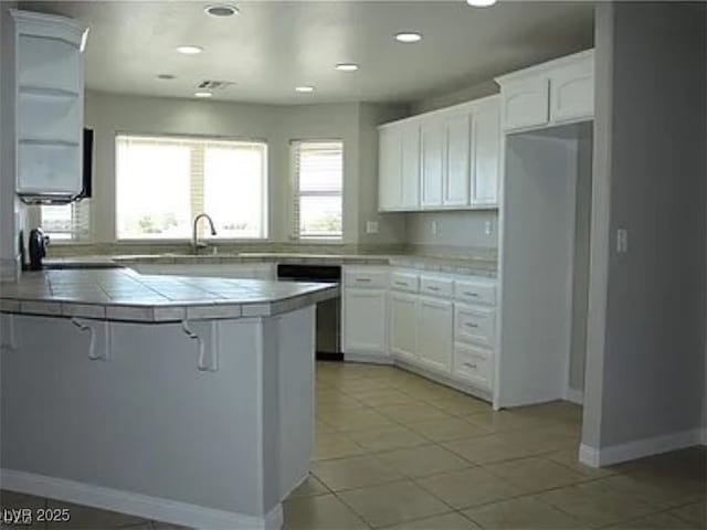 kitchen with tile counters, white cabinetry, a breakfast bar area, dishwasher, and a sink