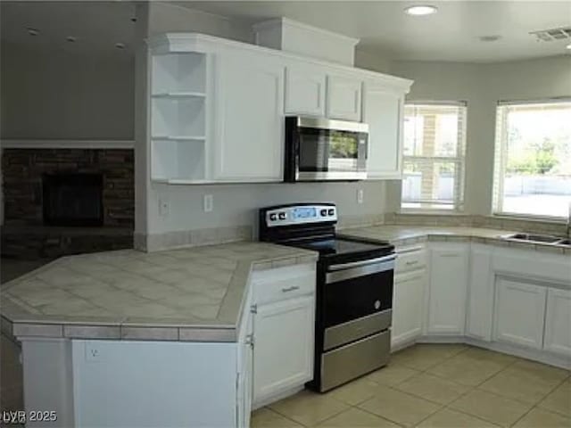 kitchen with a peninsula, open shelves, a fireplace with raised hearth, white cabinets, and stainless steel appliances