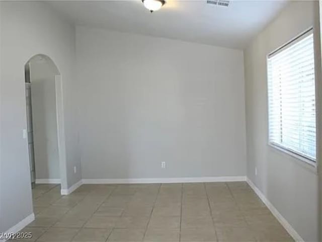 empty room with arched walkways, light tile patterned floors, baseboards, and visible vents