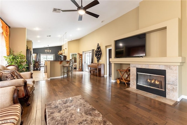 living room featuring hardwood / wood-style floors, ceiling fan with notable chandelier, a tile fireplace, lofted ceiling, and visible vents