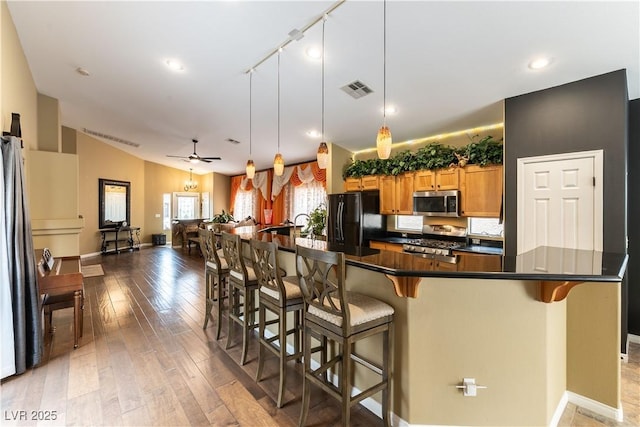 kitchen featuring stainless steel appliances, a breakfast bar, dark countertops, visible vents, and light wood-type flooring