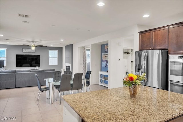 kitchen with light stone countertops, appliances with stainless steel finishes, a kitchen island, and a ceiling fan