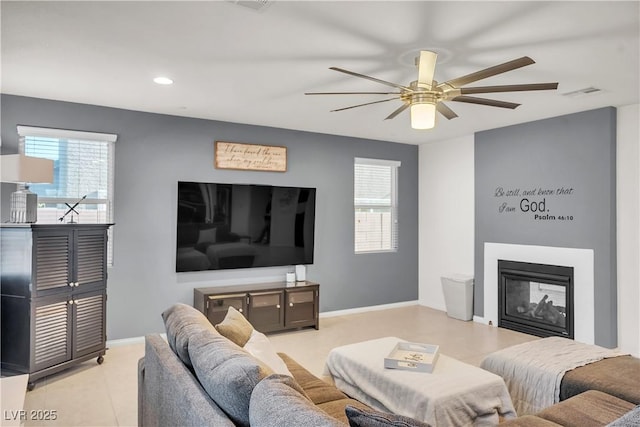tiled living room with a multi sided fireplace, visible vents, a ceiling fan, and a healthy amount of sunlight