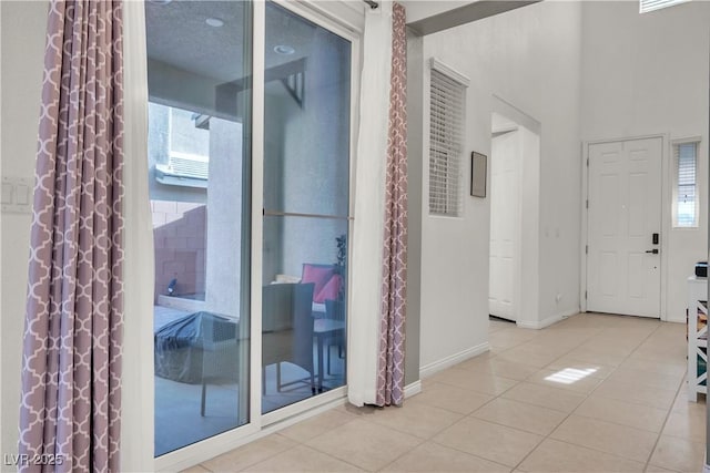 interior space featuring light tile patterned floors, a towering ceiling, and baseboards