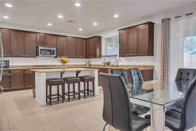 kitchen with stainless steel microwave, a kitchen breakfast bar, a center island, and light stone countertops