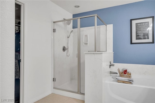bathroom featuring a walk in closet, tile patterned floors, a shower stall, and a garden tub