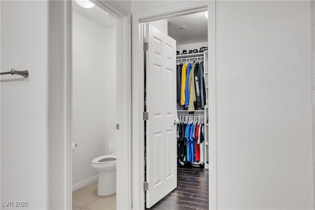 bathroom featuring toilet, a spacious closet, wood finished floors, and baseboards