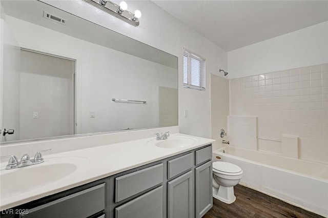 bathroom featuring toilet, wood finished floors, a sink, and visible vents