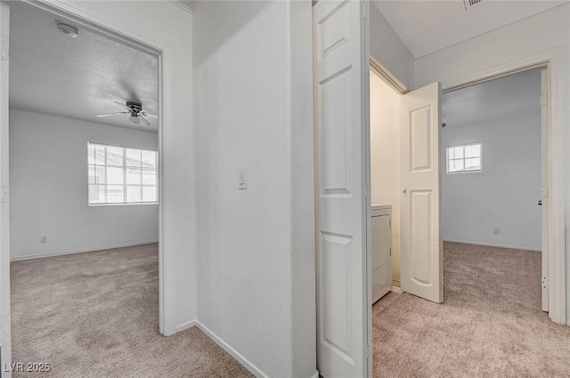 hallway featuring washer / clothes dryer, baseboards, and light carpet