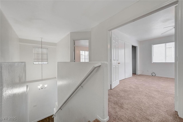 corridor featuring a chandelier, carpet flooring, an upstairs landing, and plenty of natural light