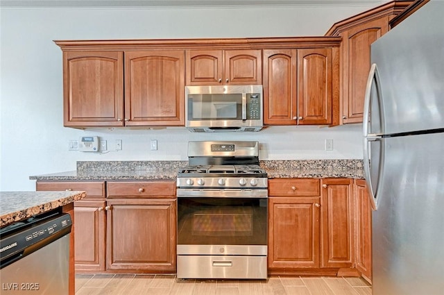 kitchen with stainless steel appliances, wood finish floors, brown cabinets, and light stone counters