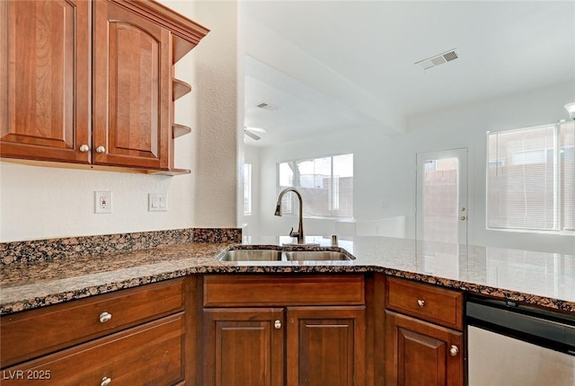 kitchen with a sink, visible vents, brown cabinetry, and dark stone countertops