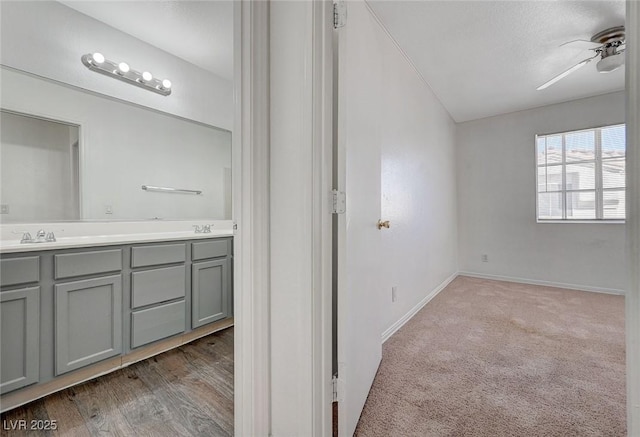bathroom with a ceiling fan, wood finished floors, a sink, double vanity, and baseboards