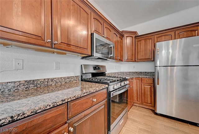 kitchen with brown cabinets, stone counters, appliances with stainless steel finishes, and wood tiled floor