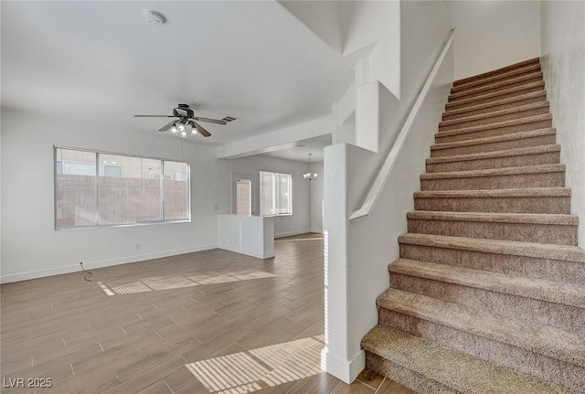 stairway with a wealth of natural light, ceiling fan with notable chandelier, baseboards, and wood finished floors