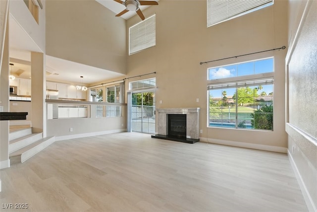 2445 Antler Point Dr, Henderson, NV 89074 - unfurnished living room featuring light wood-type flooring, a high end fireplace, a towering ceiling, and ceiling fan