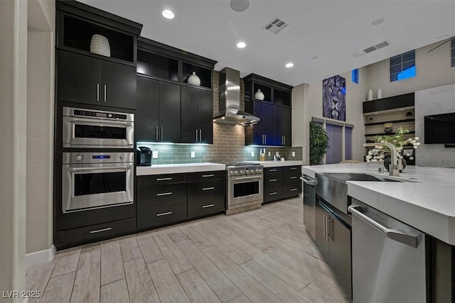 10 Olympia Outlook Dr, Las Vegas, NV 89141 - kitchen with tasteful backsplash, dark cabinets, light wood-style floors, appliances with stainless steel finishes, and wall chimney range hood